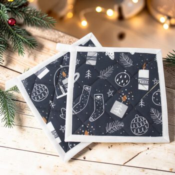 Dunkelblauer Weihnachts-Topflappen mit weißen Tannenbäumen, Christbaumkugeln, Kerzen und Sternen, dekorativ auf einer Holzfläche arrangiert.