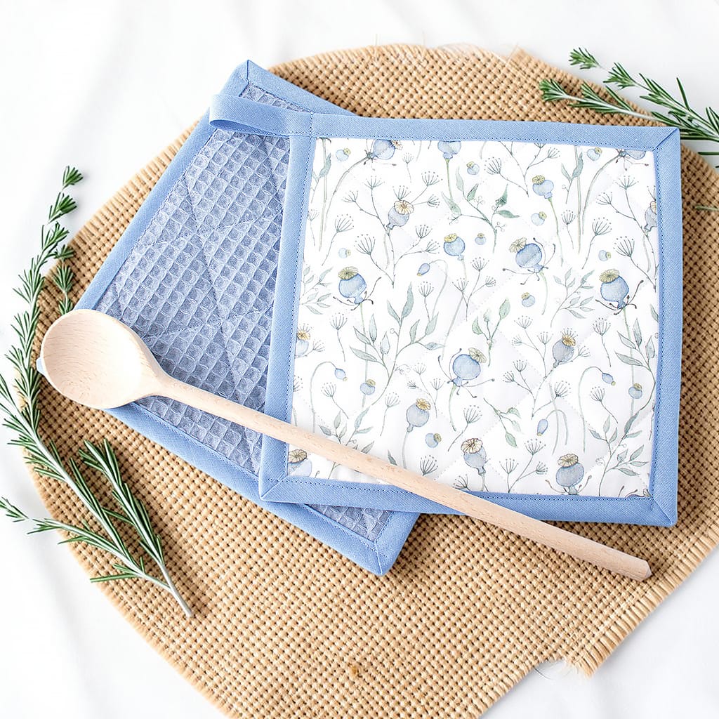 Zwei Topflappen mit weißem Mohnblumen-Stoff und hellblauer Einfassung, passend für eine stilvolle Küche