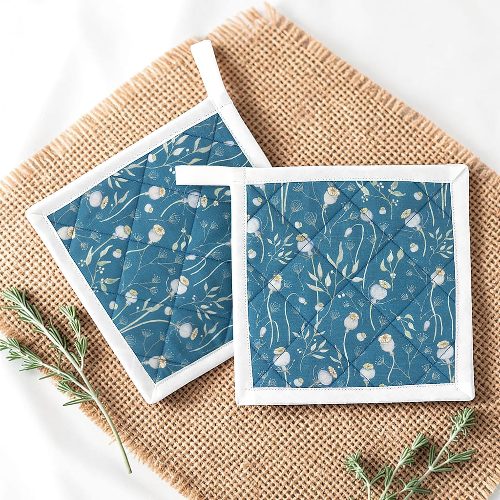 Zwei blaue Topflappen mit feinem Mohnblumen-Muster und weißer Einfassung, auf einem Jutestoff arrangiert