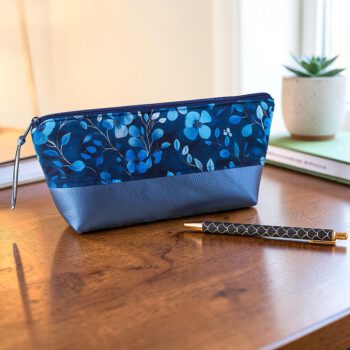 Handgefertigtes Federmäppchen aus blauem Blumenstoff und dunkelblauem Kunstleder auf einem Holzschreibtisch mit Kugelschreiber.