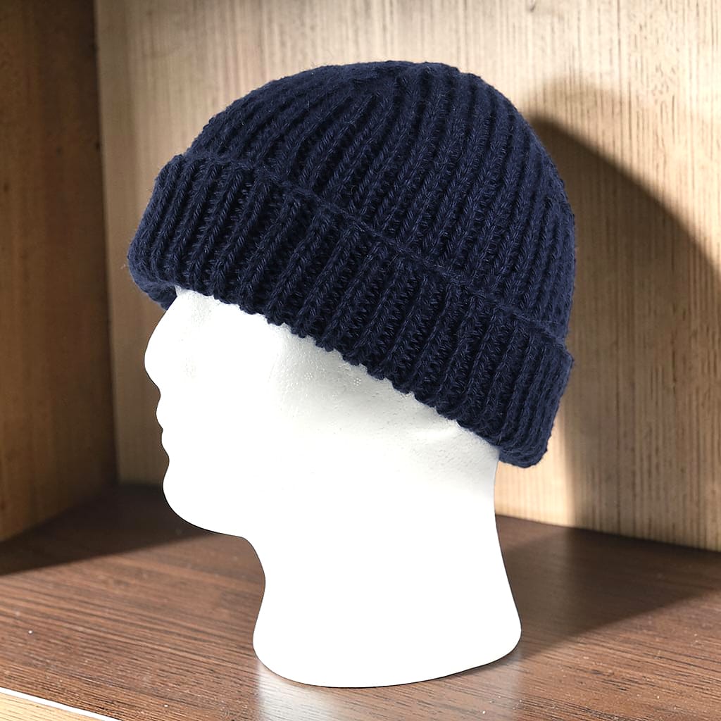 Handgestrickte dunkelblaue Mütze aus Baby Alpaka sitzt auf einem weißen Modellkopf und bedeckt Kopf und Ohren, Seitenansicht.