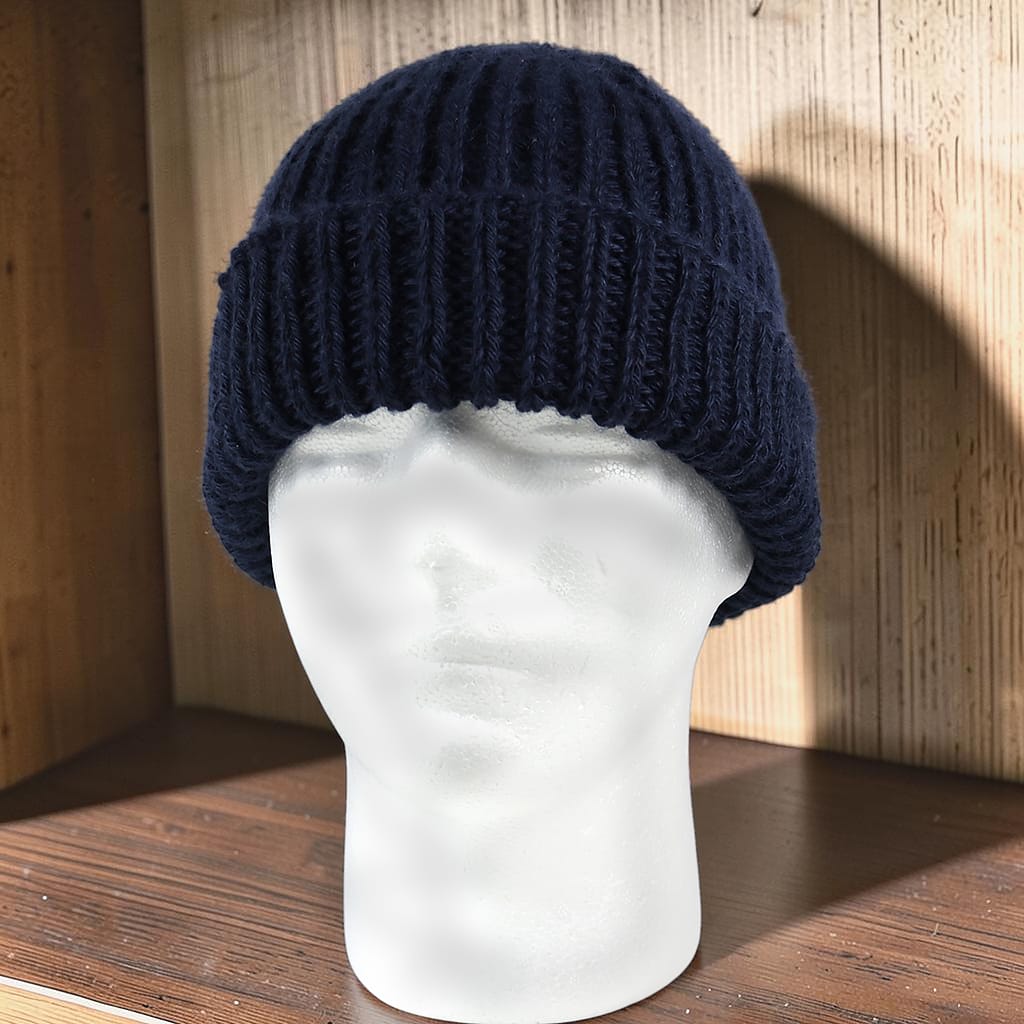 Handgestrickte dunkelblaue Mütze aus Baby Alpaka mit breitem geripptem Bündchen sitzt auf einem weißen Modellkopf, Vorderansicht.