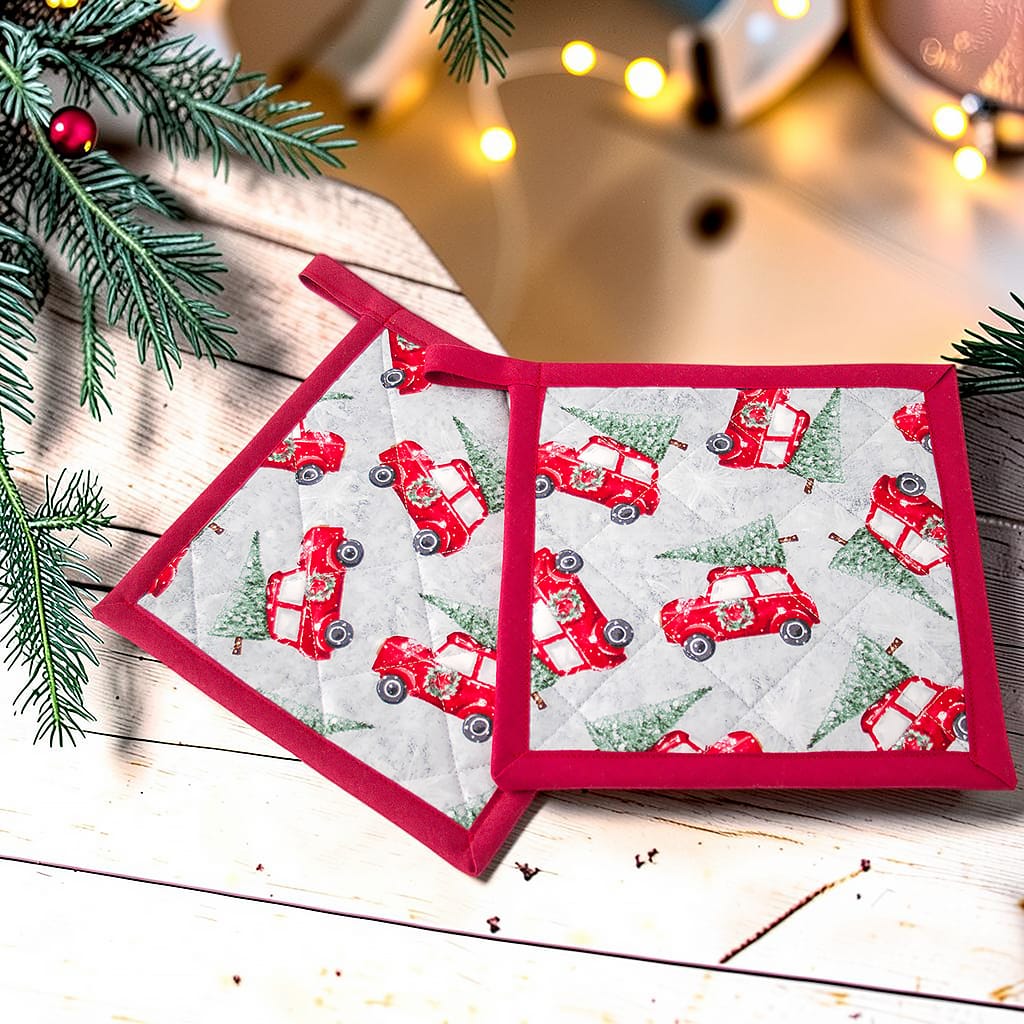 Handgemachte Topflappen mit roten Weihnachtsautos und Tannenbäumen, dekorativ auf weißem Holzhintergrund mit Tannenzweigen